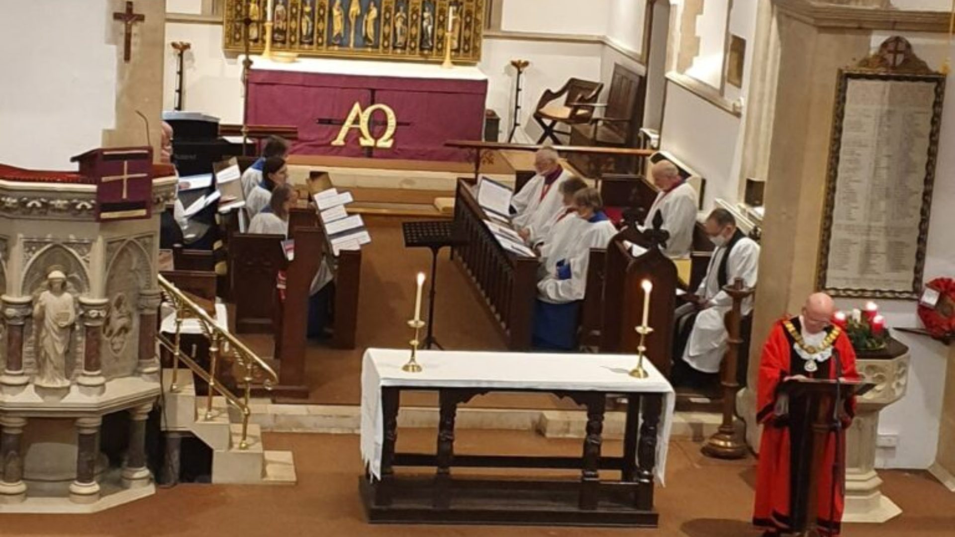 Internal of a church: Thatcham Mayor standing at a lectern whilst a choir sits in the choir stalls behind