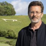 A photo of JS Monroe standing in front of a chalk white horse on a green hill