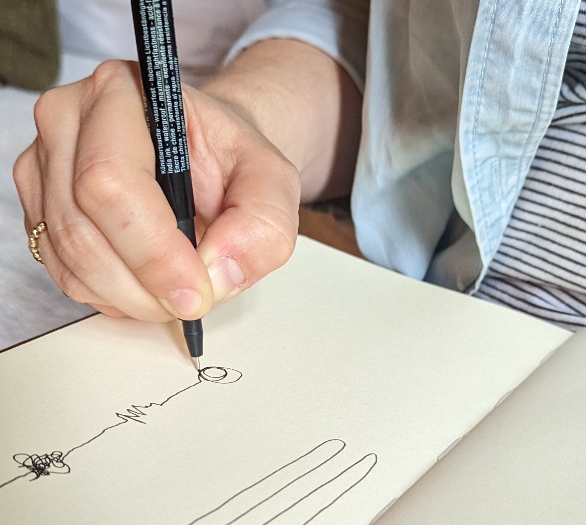 A hand holding a black pen doodles in a notebook